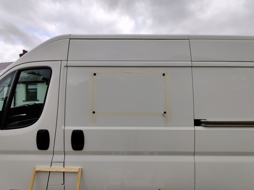 The side of the van with four holes cut in the corners of what would become the window opening